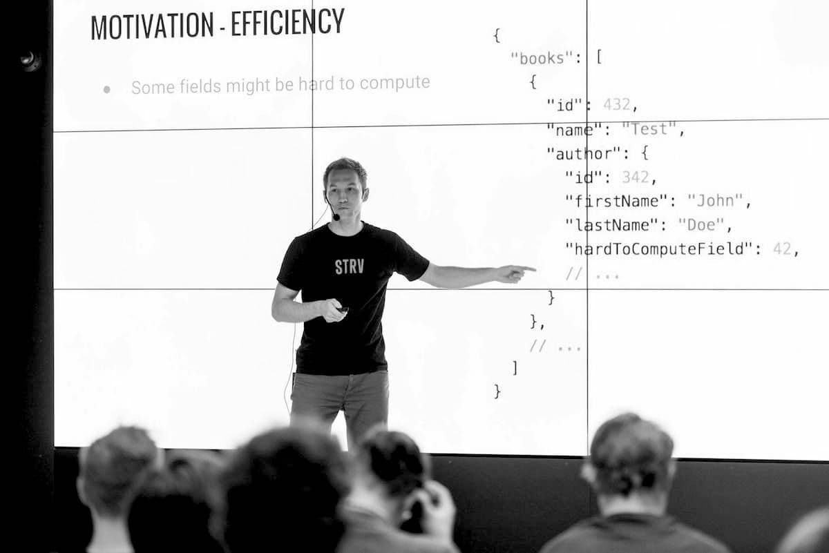 A presenter gestures towards a screen displaying a code snippet about book data structure during a talk on efficiency.