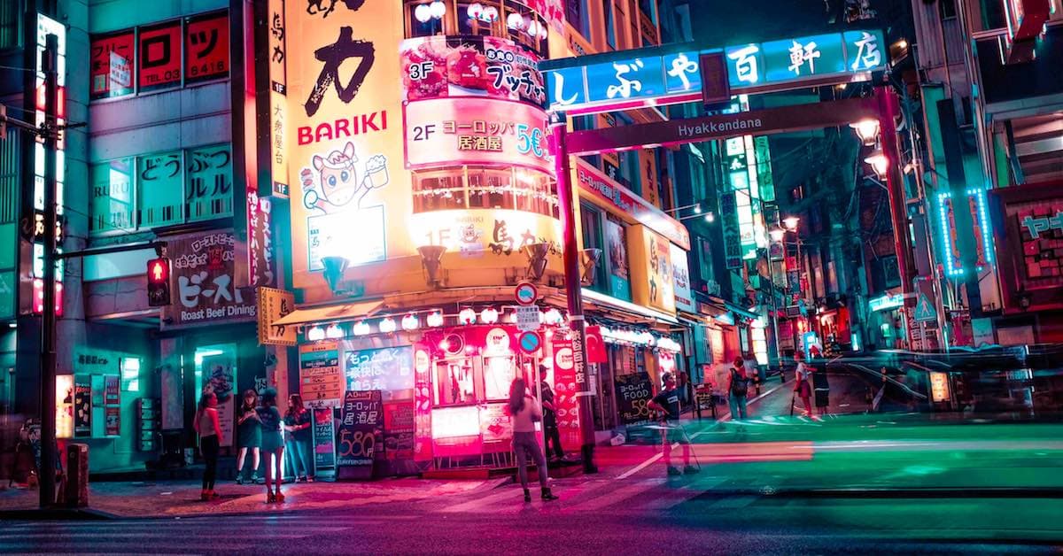 Neon-lit street scene in Tokyo with restaurants and pedestrians, showcasing vibrant signage and colorful lights at night.