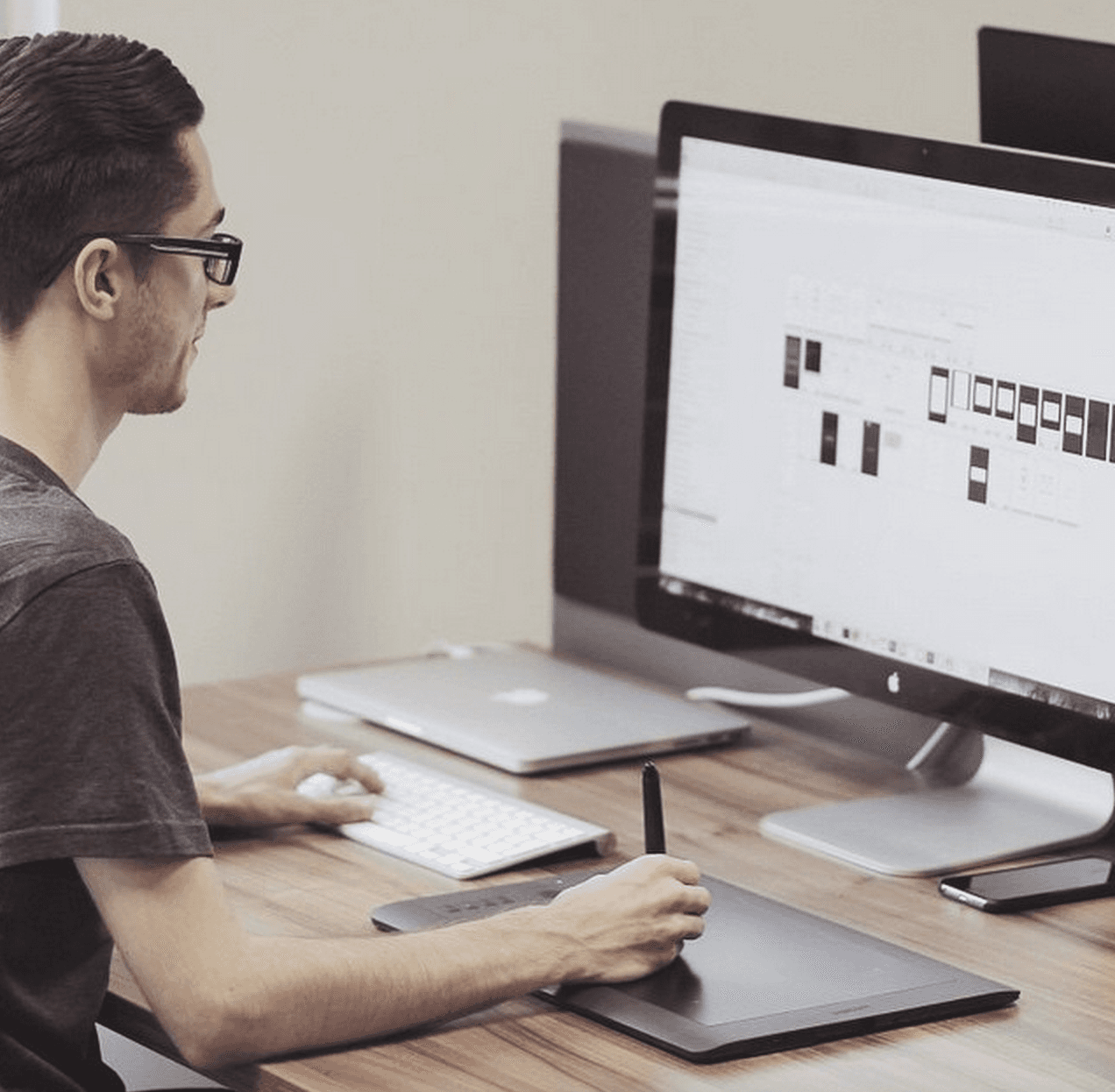 A person with glasses uses a drawing tablet while working on a computer, which displays a design layout.