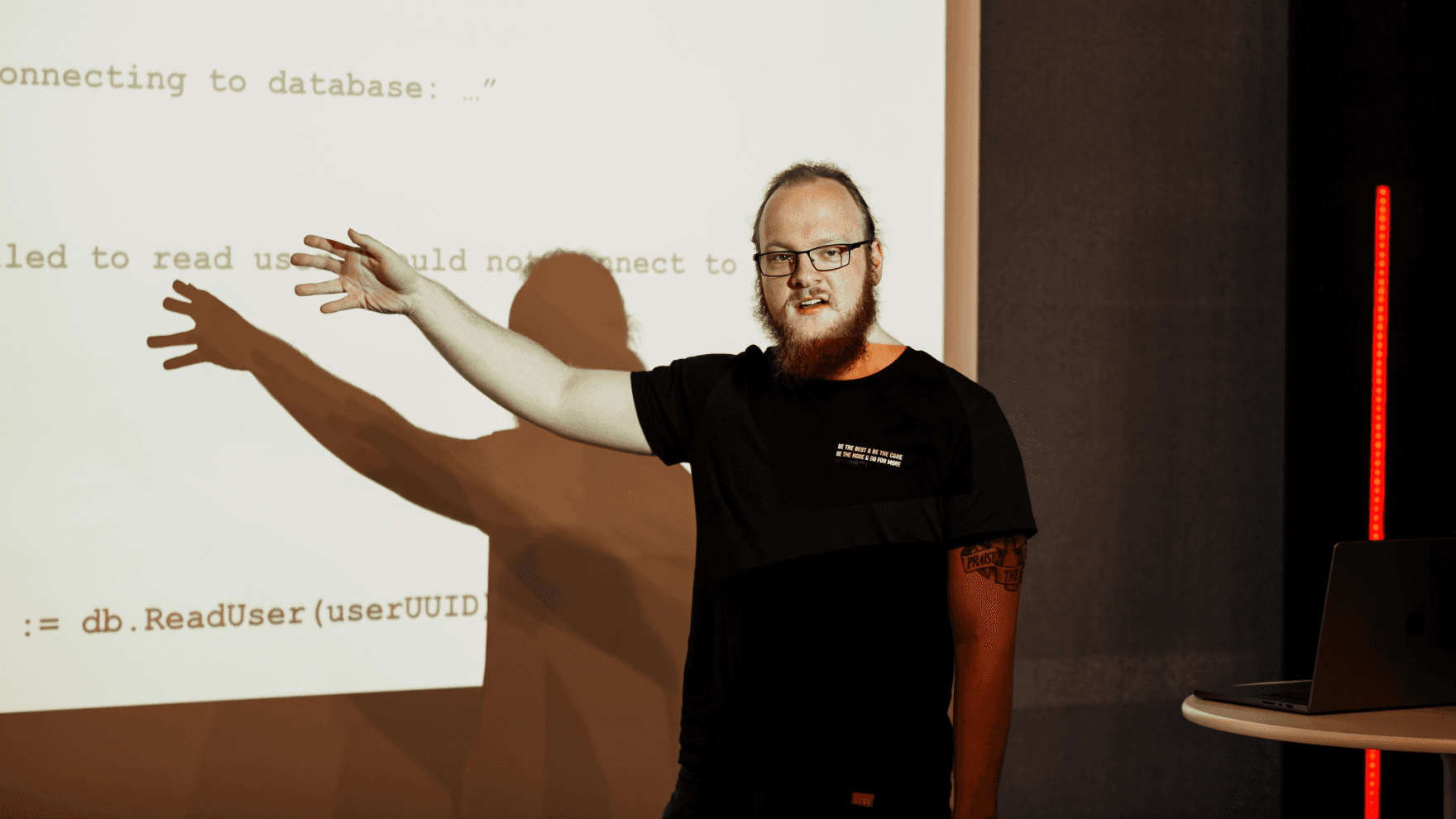 A presenter gestures toward code on a screen, discussing database connectivity issues during a lecture or workshop.